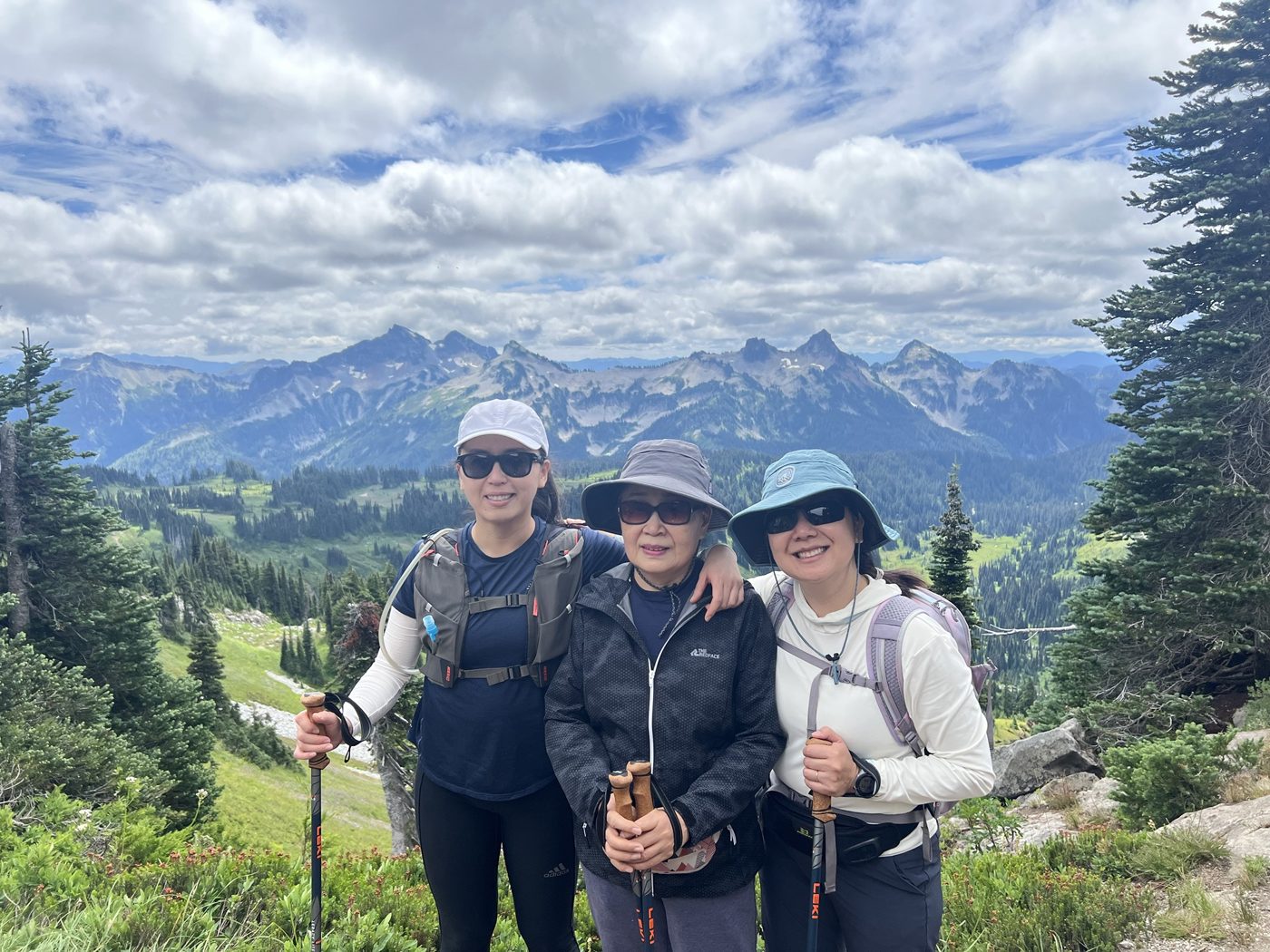 Miae hiking in the mountains with her two daughters, all smiling in sun hats with trekking poles
